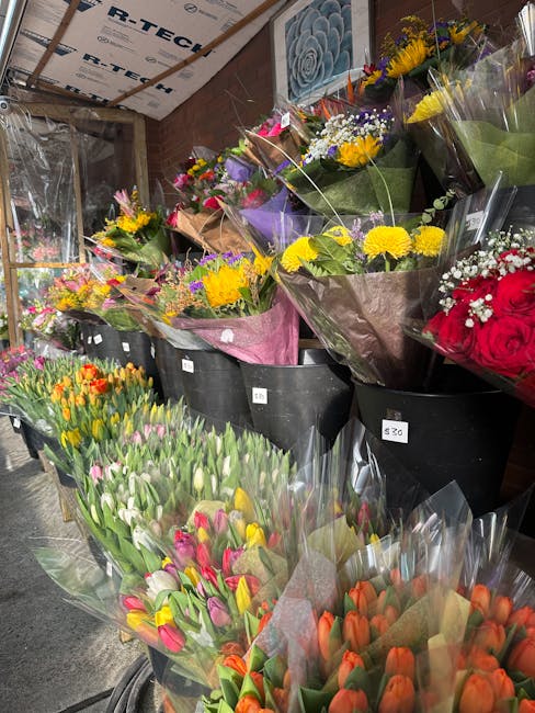 A display of various fresh floral arrangements and bouquets arranged in black buckets at a flower shop. The bouquets feature vibrant spring flowers such as tulips, daisies, roses, and mixed wildflower