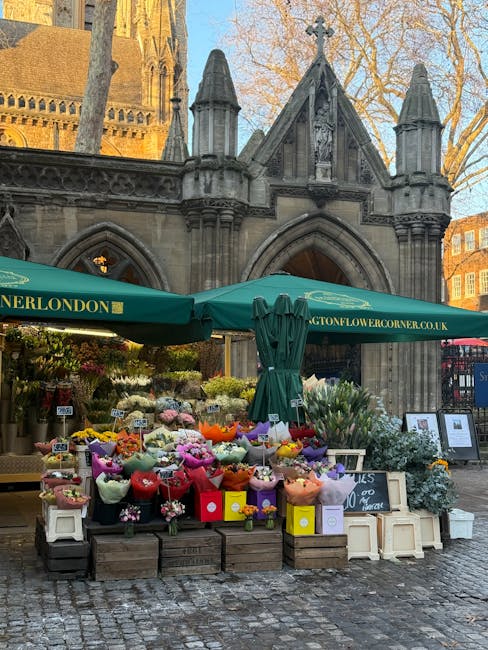 An outdoor flower stall set up in front of a historic stone building with Gothic architectural features, including arched windows and decorative spires. The stall, branded with 'Addington Flower Corne